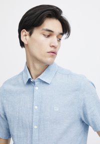 Camicia button-up azzurro chiaro in tessuto misto lino, maniche corte, colletto classico e un piccolo logo ricamato sul lato sinistro del petto.