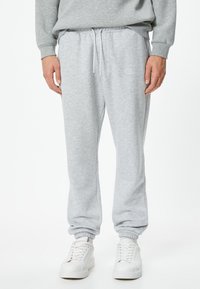 Lys grå sweatpants lavet af blødt stof, med elastisk talje med snøre og tætsiddende cuffs, parret med hvide sneakers.
