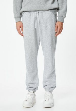 Lichtgrijze sweatpants gemaakt van zachte stof, met een elastische tailleband met trekkoord en taps toelopende boorden, gecombineerd met witte sneakers.