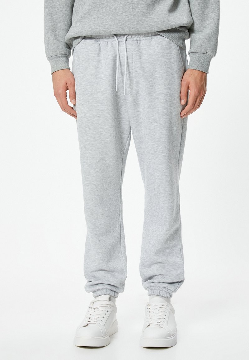 Lys grå sweatpants lavet af blødt stof, med elastisk talje med snøre og tætsiddende cuffs, parret med hvide sneakers.