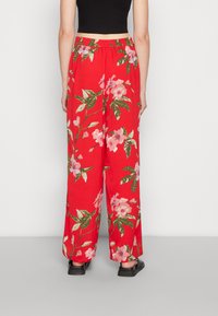Calças largas vermelhas com padrão floral, com um cinto elástico, apresentando padrões de flores rosas e verdes, feitas de um tecido leve.