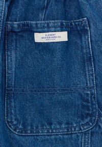 Denim tkanina v bogati modri barvi, z pravokotno žepom in belim oznako, ki navaja "ELEMENT SKATEBOARD CO." z modrim besedilom.