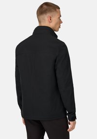 Giacca softshell nera con colletto alto, maniche lunghe e una superficie liscia e opaca. Design minimalista, cuciture eleganti e polsini regolabili.