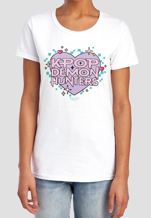 White t-shirt with large purple heart design and text "KPOP DEMON HUNTERS" in pink, worn by a person in light blue jeans.