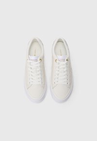 White leather sneakers with round toe, textured sides, gold eyelets, and white laces. Thick white outsole with subtle color accents.