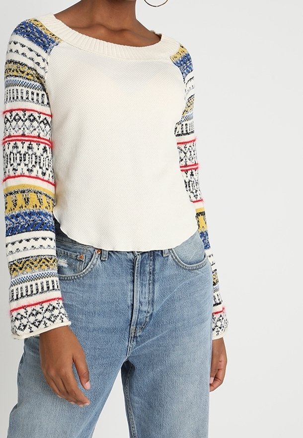 Neulepusero, jossa on voi-valkoinen vartalo ja värikkäät kuviolliset hihat sinisessä, keltaisessa, punaisessa ja mustassa. Varustettu ribatusta pääntiestä ja tekstuuripintaisesta kankaasta.