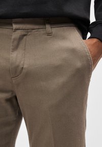 Beiget puuvillahousut, joissa on sileä pinta, kapea malli, sivutaskut ja suora etuosa.