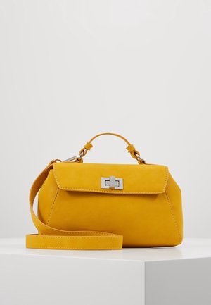 Sac à main jaune moutarde avec poignée supérieure, fermoir à tourniquet argenté et bandoulière longue amovible sur une surface blanche contre un fond uni.