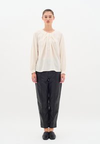 Blusa color crema con maniche a palloncino e scollatura arricciata, abbinata a pantaloni in pelle nera attillati e scarpe nere semplici.