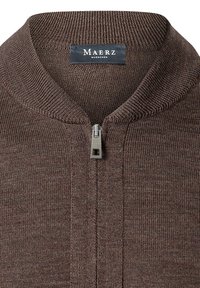 Suéter marrón de cremallera con un cuello acanalado, tela de punto texturizada y una cremallera de metal. La etiqueta dice "MAERZ Muenchen."