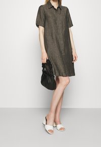 Lyhythihainen, kaulallinen mekko tummanruskeaa pellavaa, jossa on rento malli. Yhdistetty mustan käsilaukun ja valkoisten avointuippuisten, paksupohjaisten kenkien kanssa.