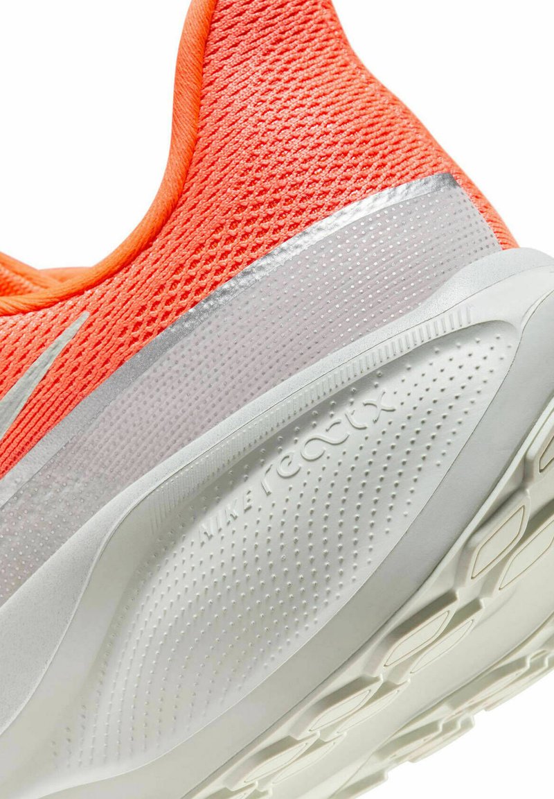 Haut en maille orange avec des accents argentés, doté d'une semelle blanche rembourrée et d'un motif de grip texturé. Marque visible sur le talon.