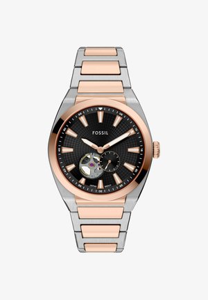 Montre Fossil avec un cadran rond noir, des accents en or rose et un bracelet en acier inoxydable argenté. Présente un mouvement squelettique et un motif texturé.
