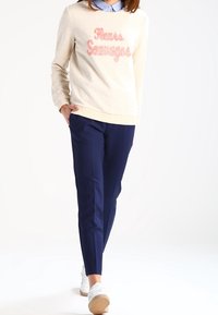 Sweatshirt crème avec un texte rose disant "Fleurs Sauvages", associé à un pantalon marine et des baskets blanches, avec une texture lisse.