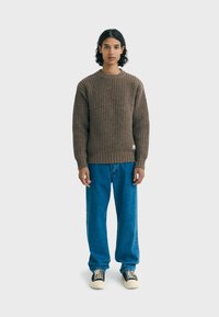 Pull en maille côtelée marron, col rond, associé à un jeans droit bleu et des baskets noires à semelles crème. Design simple et texturé.