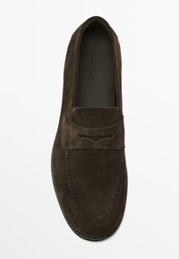 Brune ruskinds loafers med rund tå, flad sål og dekorativt syninger over det øverste. Har en subtil udskæring foran.
