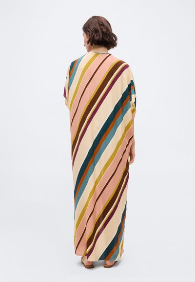 Γυναίκα με κοντά καστανά μαλλιά που φοράει μακρύ, άνετο φόρεμα με πολύχρωμες διαγώνιες ρίγες και καφέ σανδάλια, με την πλάτη γυρισμένη.
