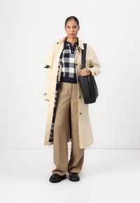 Bēša trencis, jūras zila un balta rūtainā svītera, bēša platām kājām bikses, melni masīvi apavi, melna plecu soma ar siksnu.