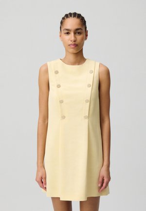 Vestido amarillo sin mangas con escote redondo, que presenta seis botones forrados de tela en la parte frontal y una falda acampanada. Textura suave.