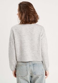 Suéter de punto gris claro con un corte relajado, hombros caídos y puños de canalé, combinado con jeans de tiro alto en azul desgastado.