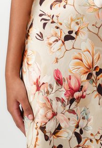 Blommig klänning med en beige bakgrund och stora magnolia- och pionmönster i rosa, krämiga och bruna nyanser; mjuk tygtextur.