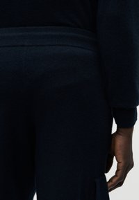 Μπλε πουλόβερ ναυτικού τύπου με απαλό, υφασμάτινο ύφασμα, ριμπ μανσέτες και χαλαρή σιλουέτα με το χέρι να ακουμπά στο πλάι.