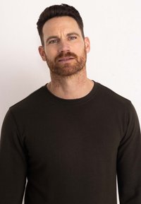 Dark green long-sleeve shirt with a crew neckline. Soft, smooth texture with visible stitching along edges. Simple design without patterns.