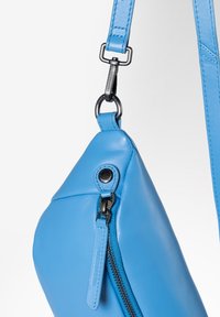 Borsa a mano in pelle blu di forma triangolare, con chiusura a zip, hardware nero e una tracolla removibile con dettagli cuciti.