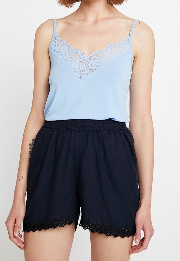 Femme portant un caraco bleu clair bordé de dentelle et un short noir taille haute avec un ourlet en dentelle festonnée.