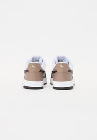 Puma Sneaker mit einem weißen und hellbraunen Design, ausgestattet mit einem gepolsterten Kragen, schwarzen Akzenten und strukturiertem Material. Schwarze Außensohle ist sichtbar.