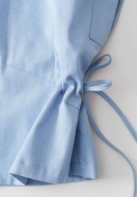 Lichtblauw overhemddetail met een gathered mouw en een gestrikte strik. Soepele stof met een subtiele textuur en een zijzak op de mouw.