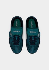 Puma sneakers in dark green and navy with textured leather, featuring a Slytherin logo on the velcro strap and patterned insoles.