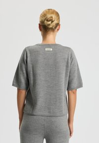 Maglione grigio a maglia con maniche corte, caratterizzato da un collo tondo e un'etichetta sul retro. Tessuto morbido e vestibilità rilassata.