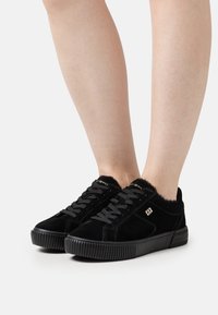 Sneaker in suede nero con superficie testurizzata, punta rotonda e suola in gomma. Presentano lacci neri e un morbido bordo in pelliccia attorno alla caviglia.