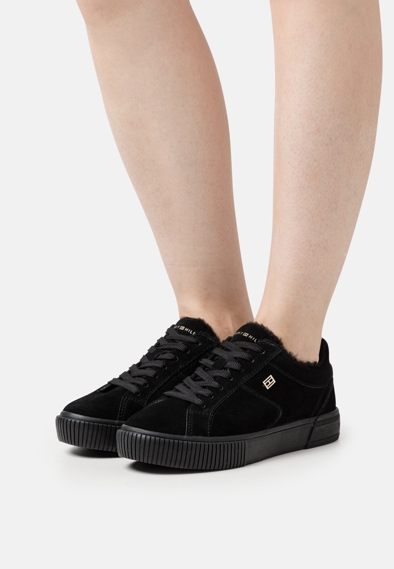 Sneaker in suede nero con superficie testurizzata, punta rotonda e suola in gomma. Presentano lacci neri e un morbido bordo in pelliccia attorno alla caviglia.