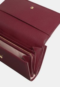 Burgundská kožená peněženka s texturovaným povrchem, s gold zapínáním a několika přihrádkami, včetně zipové sekce.