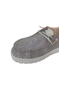 Zilveren glittersneaker met een platte, ronde neus, witte veters en een gestructureerde afwerking. Heeft een witte buitenzool en een gelabelde tong.