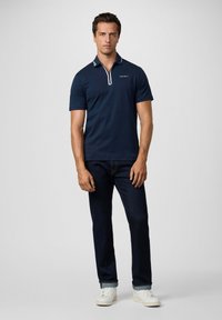 Mornarska polo majica s kratkim rukavima i zatvaračem na vratu, s bijelim detaljima na ovratniku. Uparena s tamnim trapericama i bijelim cipelama.