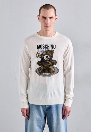 Weißer Strickpullover mit einem Grafikdesign eines Bären in Kochmütze, einem Teller und dem Text "Moschino" darüber. Weicher Stoff, gerippte Bündchen und Saum.
