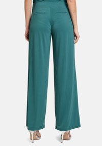 Wide-leg trousers in teal fabric, featuring a smooth texture and a high waistband with two back pockets. Paired with open-toed heels.