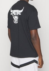 Camiseta de algodón negra con un gran gráfico de un toro blanco en la parte posterior, mangas cortas y un dobladillo recto. Adecuada para uso casual.