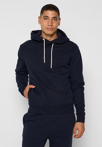 Haut à capuche bleu marine en tissu mélangé coton, avec une capuche à cordon de serrage, une poche kangourou, et des poignets et un ourlet côtelés. Design simple.