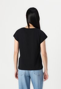 Svart bomull t-shirt med kort ärm, rund halsringning och avslappnad passform. Bärs med ljusblå jeans, vilket visar en enkel, vardaglig design.