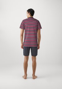 Striped short-sleeve t-shirt in burgundy, navy, and white, paired with dark gray shorts. Model stands barefoot, viewed from the back.
