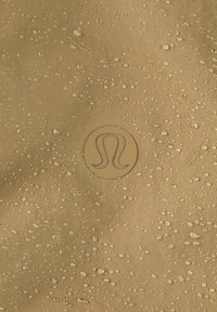 Surface texturée beige avec des gouttelettes d'eau réparties uniformément et un logo stylisé en relief "A" au centre.