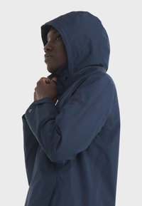 Mornarska vodootporna jakna s kapuljačom, visokim ovratnikom, podesivim vezicama i logotipom na rukavu. Glatka tekstura.