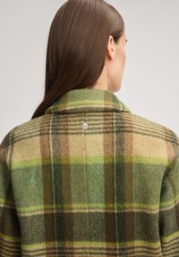 Wolljacke mit grünem und braunem Karo-Muster, mit einem Reverskragen und silbernem Knopfdetail auf der Rückseite.