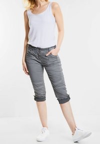 Pantalons gris courts avec un ourlet à cordon de serrage, des poches, et une coupe slim, associés à un débardeur blanc et des baskets blanches.