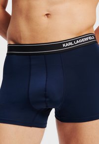 Mornarsko plavi bokserice s crnim pojasom na kojem je bijelim slovima napisano "KARL LAGERFELD". Glatki materijal s kontrastnim prošivima.