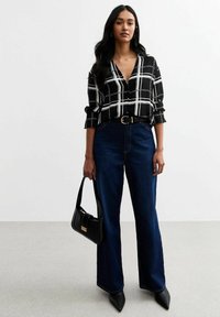 Blusa a righe bianco e nero con scollo a V, abbinata a jeans larghi in denim scuro a vita alta, borsa nera e tacchi a punta.